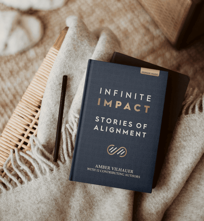 Infinite Impact Anthology book on top of chair, next to a pencil with a cozy and warm background